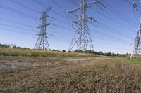 three electric towers in grassy area next to a dirt road and woodside road, with two people standing on one