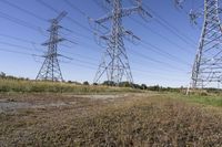 three electric towers in grassy area next to a dirt road and woodside road, with two people standing on one