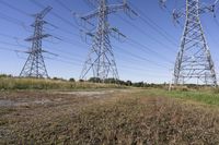 three electric towers in grassy area next to a dirt road and woodside road, with two people standing on one