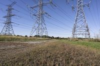 three electric towers in grassy area next to a dirt road and woodside road, with two people standing on one