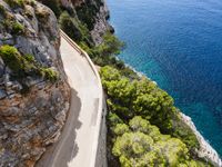 winding road next to the beach with sea and trees surrounding it and a mountain cliff in the back ground