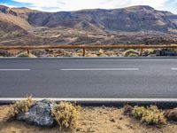 a desert with rocky terrain and an asphalt road next to it is a metal fence