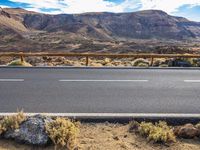 a desert with rocky terrain and an asphalt road next to it is a metal fence
