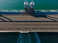 a bridge over the ocean with construction equipment in the background and two people walking on it