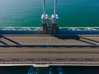 a bridge over the ocean with construction equipment in the background and two people walking on it