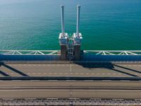 a bridge over the ocean with construction equipment in the background and two people walking on it