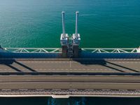 a bridge over the ocean with construction equipment in the background and two people walking on it