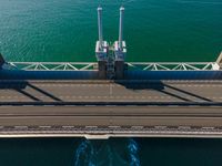 a bridge over the ocean with construction equipment in the background and two people walking on it