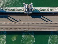 overhead shot of an elevated bridge in the ocean water, taken from above, which is visible to be a construction structure that supports a pedestrian - like a boat's