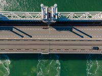 overhead shot of an elevated bridge in the ocean water, taken from above, which is visible to be a construction structure that supports a pedestrian - like a boat's