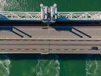 overhead shot of an elevated bridge in the ocean water, taken from above, which is visible to be a construction structure that supports a pedestrian - like a boat's