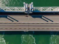 overhead shot of an elevated bridge in the ocean water, taken from above, which is visible to be a construction structure that supports a pedestrian - like a boat's