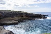 a man walking by the water in front of rocks on a cliff face down at the ocean