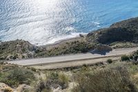 a long winding road on a cliff with water in the background and a beach below