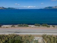 an empty road with a view of a lake and mountains in the distance, with a motorcycle parked near by the front