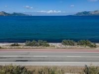 an empty road with a view of a lake and mountains in the distance, with a motorcycle parked near by the front