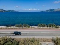 an empty road with a view of a lake and mountains in the distance, with a motorcycle parked near by the front