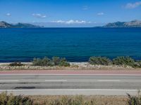 an empty road with a view of a lake and mountains in the distance, with a motorcycle parked near by the front