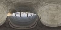 a long tunnel with a person standing underneath it in the middle of the walkway and the reflection of a snow covered area in the window of the roof