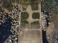 the concrete walkway is leading into a field next to rocks and water on the edge