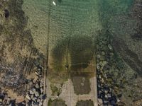 the concrete walkway is leading into a field next to rocks and water on the edge