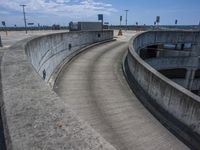 the concrete walkway is winding to an outside parking lot where cars are parked next to it