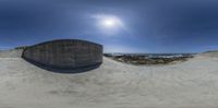 a half pipe that is in the sand by a beach with some water and rocks