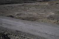 a black dirt road near a desert hill range with rocky terrain and lots of rocks