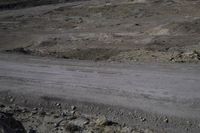 a black dirt road near a desert hill range with rocky terrain and lots of rocks