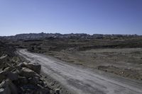 a gravel road leading towards a mountain in the distance are boulders and boulders, and a blue sky