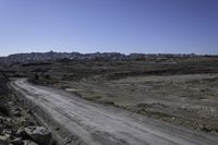 a gravel road leading towards a mountain in the distance are boulders and boulders, and a blue sky