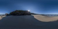 a large rock in the sand by the ocean with a setting sun behind it on a sunny day