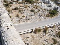 a person rides an empty, long bike near a road and cliff formation on a sunny day