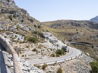 a person rides an empty, long bike near a road and cliff formation on a sunny day