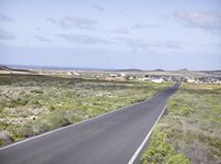 a long, empty road in the open land near the coast area with buildings on each side