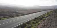 a car driving on a narrow highway through the mountains past other mountains and shrubs in a wide open landscape