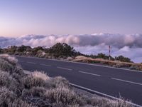 an empty winding road on a mountain with the sun set above the mountains in the background