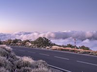 an empty winding road on a mountain with the sun set above the mountains in the background