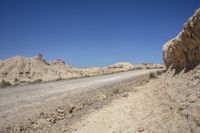 a dirt road going through a wide sandy area with rocks and boulders on both sides