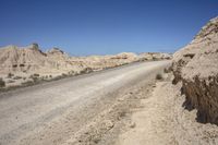 a dirt road going through a wide sandy area with rocks and boulders on both sides