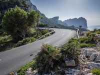 a mountain road near the sea and trees on the side of a hill side with tall rock formations