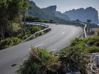 a mountain road near the sea and trees on the side of a hill side with tall rock formations