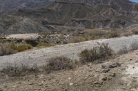 man riding a white and yellow motorcycle across a mountain side road in front of a rocky outcrop