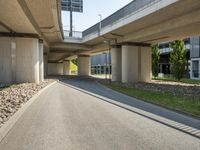 the road near a building has a very long walkway below it that crosses over an elevated overpass