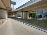 the road near a building has a very long walkway below it that crosses over an elevated overpass