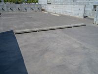 the empty parking lot in front of a wall with apartment buildings on it and a skateboarder on a ramp