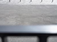 a man is in the middle of an empty parking lot with a black umbrella and two skateboards