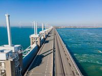 a bridge over the ocean with construction equipment in the background and two people walking on it