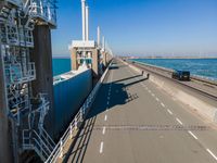 a bridge over the ocean with construction equipment in the background and two people walking on it