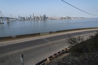 a road passing along a body of water with a city skyline in the background from an elevated view